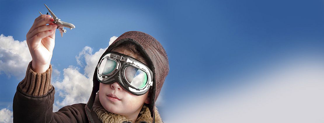 Junge mit Fliegermütze und -brille und einem Modellflugzeug