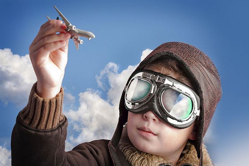 Junge mit Fliegermütze und -brille und einem Modellflugzeug