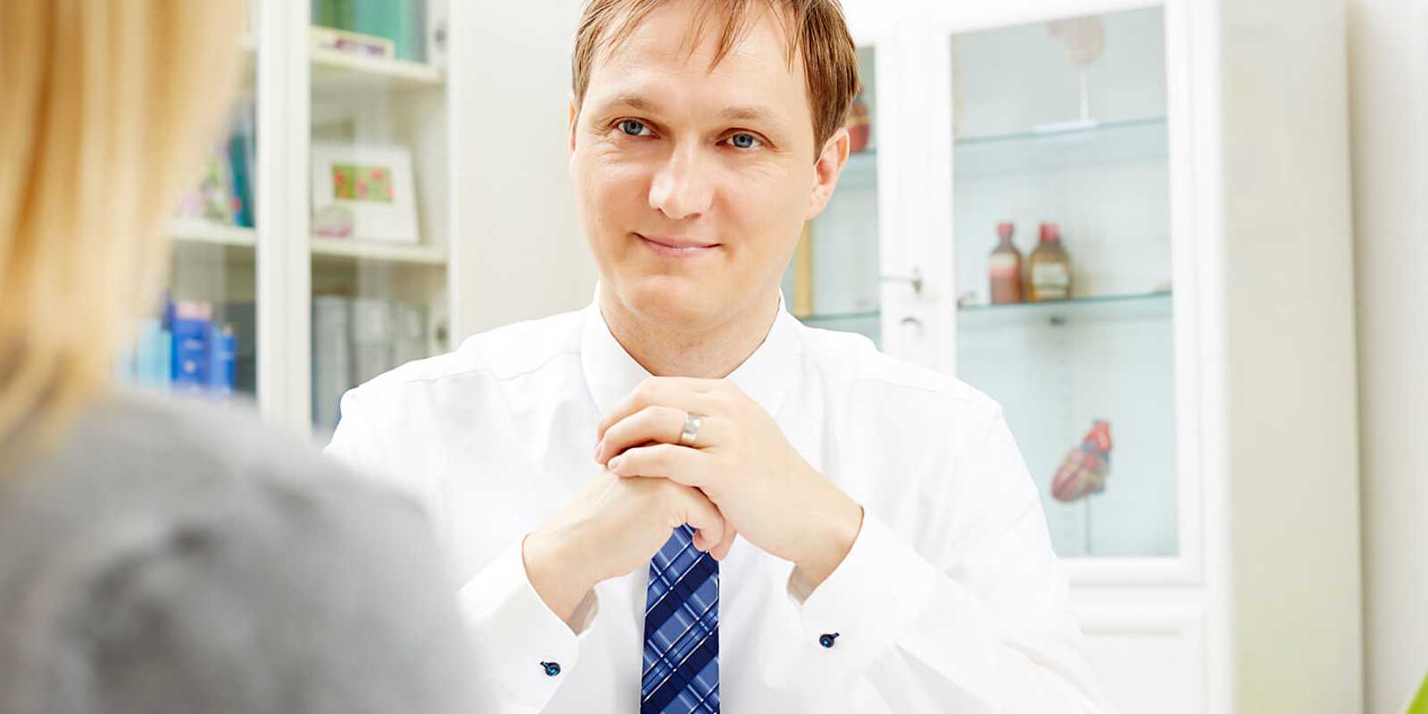 Dr. Samusch sitzt lächelnd an seinem Schreibtisch