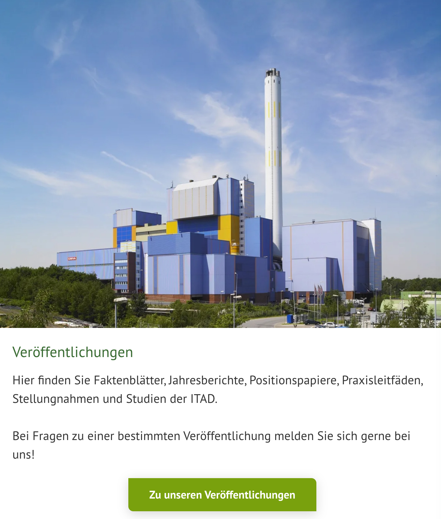 Eine große Fabrik mit einem weißen Schornstein und bunten Gebäuden, umgeben von viel Grün unter blauem Himmel.