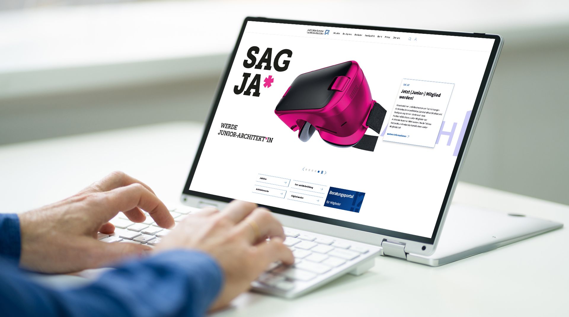 Person, die auf einem Laptop tippt und eine Website mit einer roten VR-Brille und dem Text "SAG JA*" anzeigt.