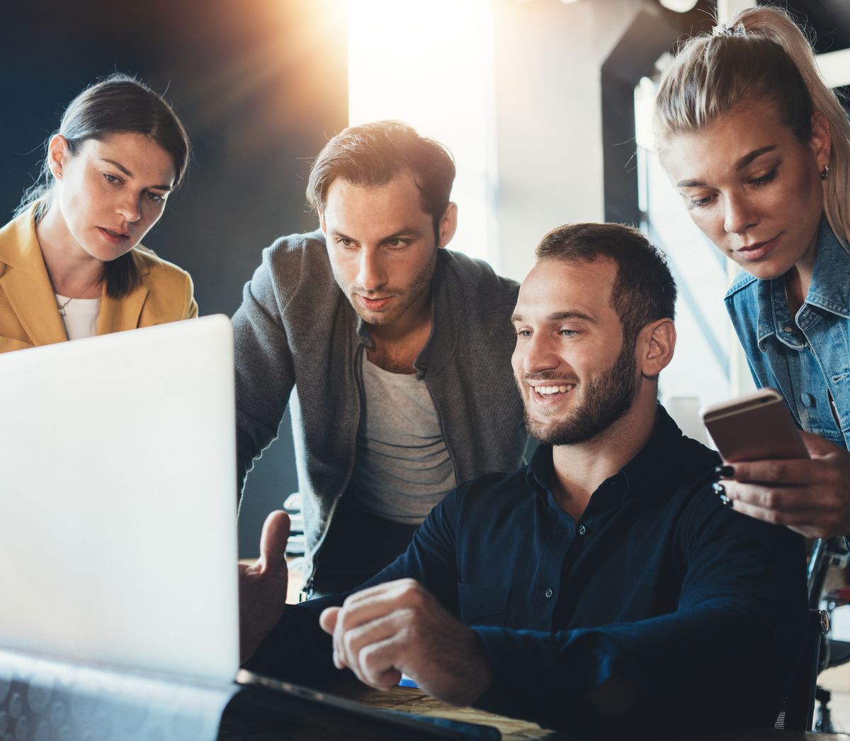 Vier Kollegen haben sich um einen Laptop versammelt, arbeiten zusammen und diskutieren mit Interesse und Enthusiasmus über etwas.