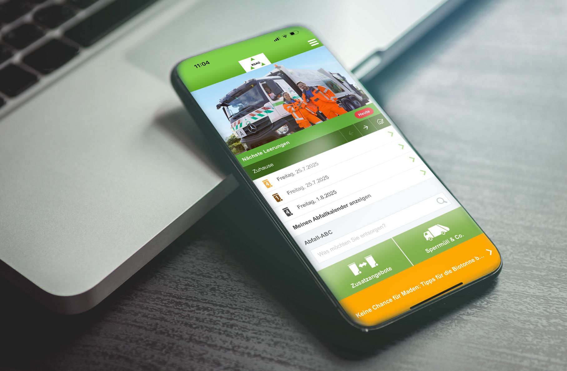 Smartphone auf einem Laptop, das eine Recycling-App mit einem Zeitplan für die Müllabfuhr und ein Foto von Müllmännern zeigt.
