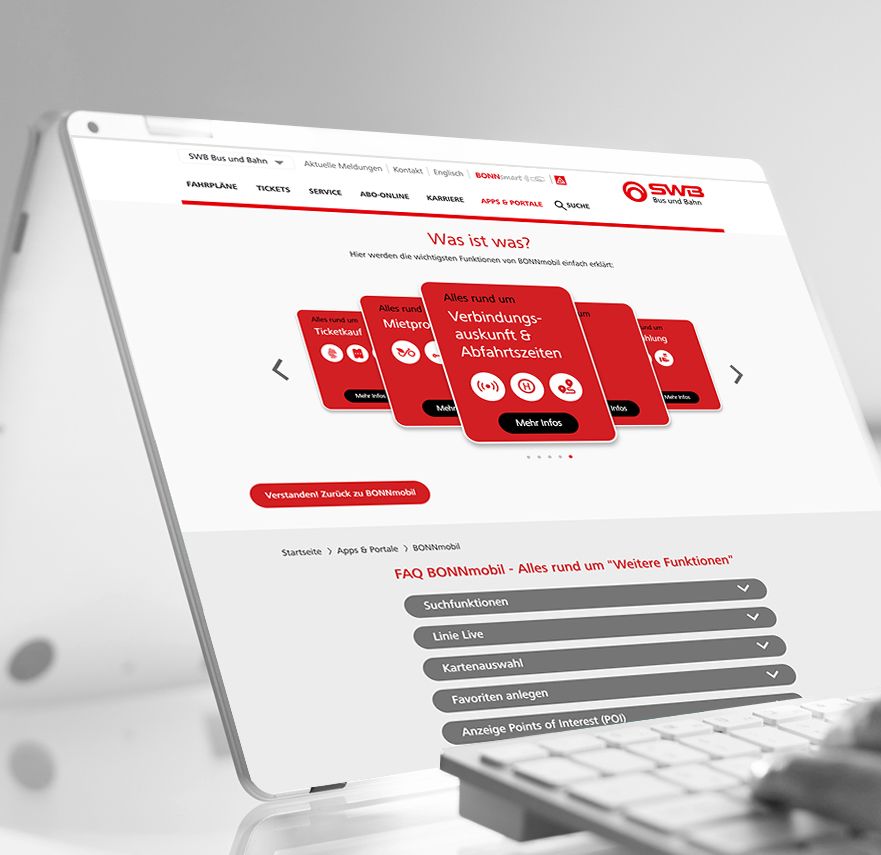 Eine Person tippt auf einer Tastatur vor einem Computer, der eine rot-weiße Website anzeigt.